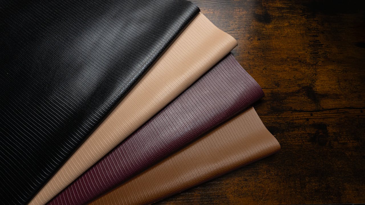 High-quality textured leather fabrics in various colors on a rustic wooden surface.
