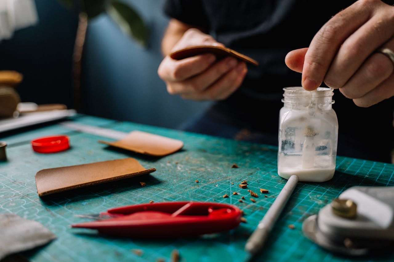 Close-up of artisan hands crafting leather, showcasing tools and materials in the workspace.